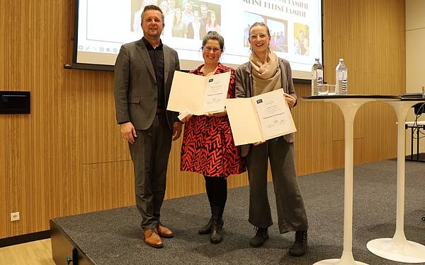 Ein Mann und zwei Frauen posieren auf einer Bühne für ein Foto