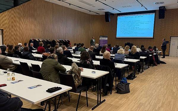 Ein Saal von hinten, vorne wird eine Präsentation auf einer Leinwand gezeigt