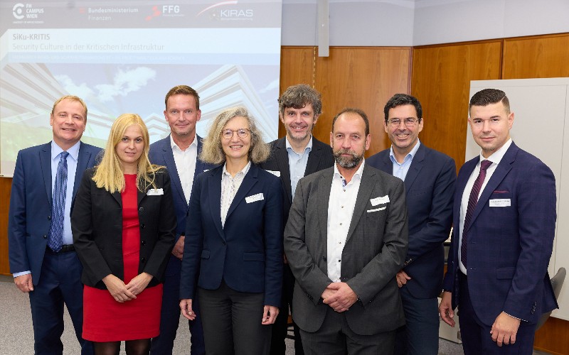 Acht Personen posieren vor einer Leinwand für ein Foto