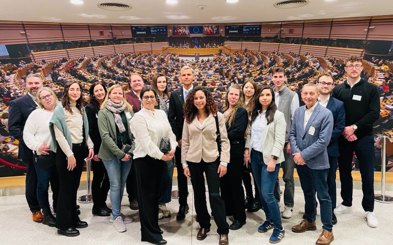 Eine Gruppe Menschen posiert für ein Bild, im Hintergrund ist das Europäische Parlament zu sehen